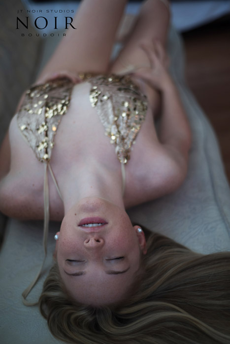 boudoir photograph of a girl in gold lingerie lying back on a couch