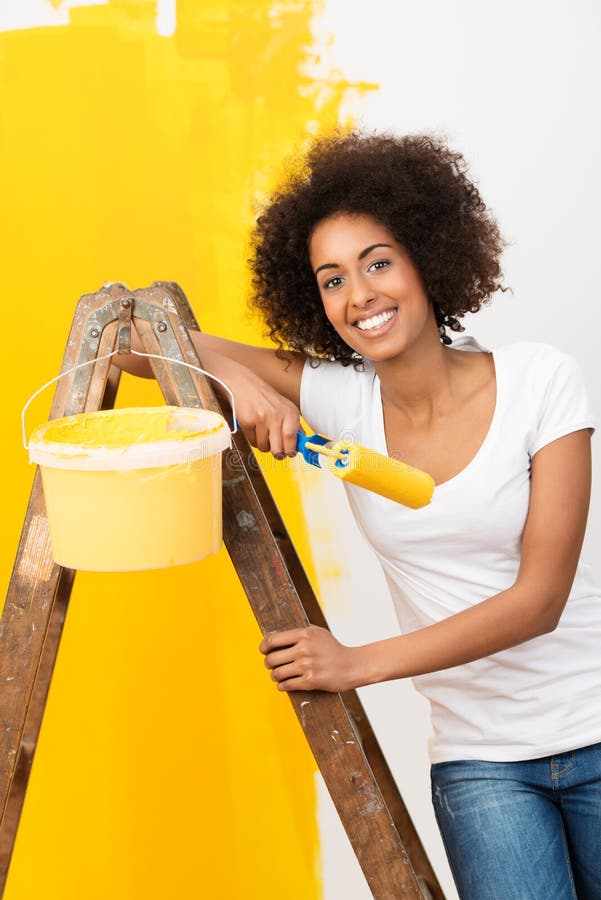 African American woman doing home renovations. Beautiful young African American woman with a lovely smile doing home renovations standing on a wooden stepladder stock photos