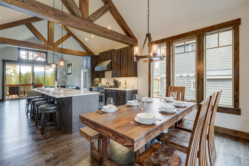 Amazing dining room near modern and rustic luxury kitchen with vaulted ceiling and wooden beams, long island with white quarts. Countertop and dark wood stock images