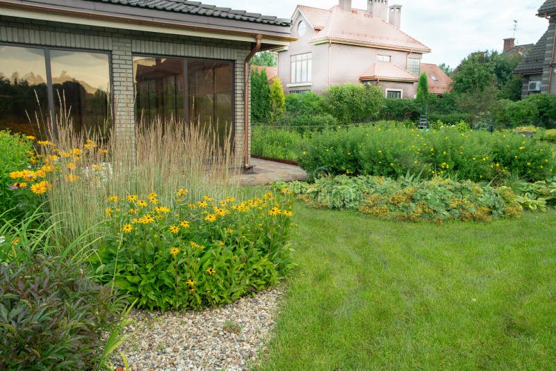 Amazing garden with perennials and grass meadow near dacha  in `Belgian village`. A magnificent garden with perennials and a country house neighboring in a royalty free stock image