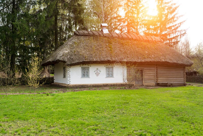 An ancient historical house in the village. A white building with yellow shutters on the windows and a roof made of straw. stock photography