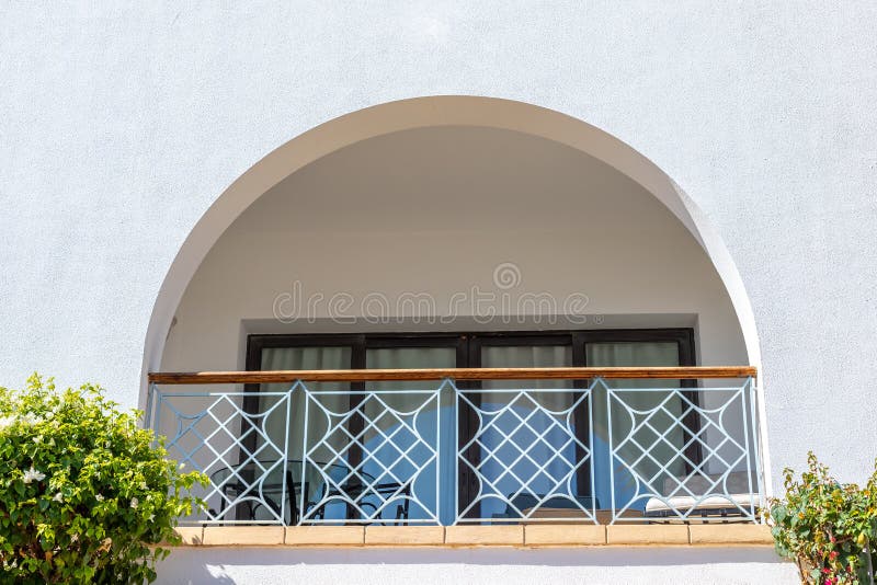Arch terrace with table and sunbeds. A semicircular window at hotel balcony. Curtains drawn up on the balcony. White wall, green. Bushes and a balcony arch with royalty free stock photo