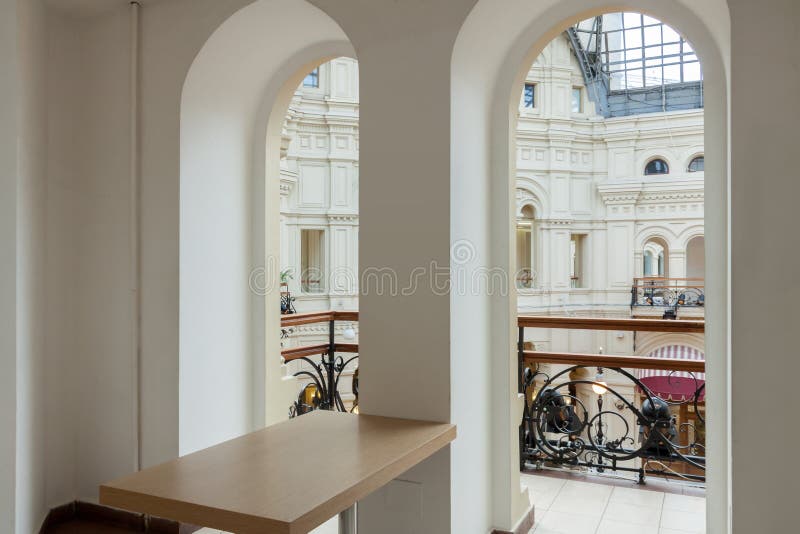 Arch white balcony wall with empty wooden table in the corner with tin railing and city building view background. Arch white balcony wall with empty wooden stock photography