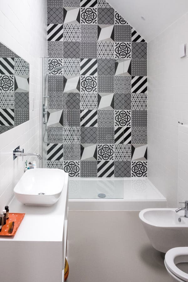 Bathroom with shower unit, toilet, bidet and basin unit, with black and white monochrome patchwork tiles and high ceiling stock images