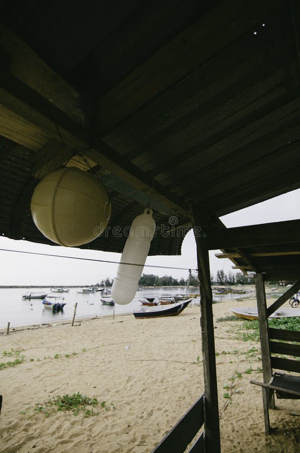 Beach scenery view from inside fisherman cottage with white and yellow buoy hanging. Anchored boat and sandy beach at morning royalty free stock image