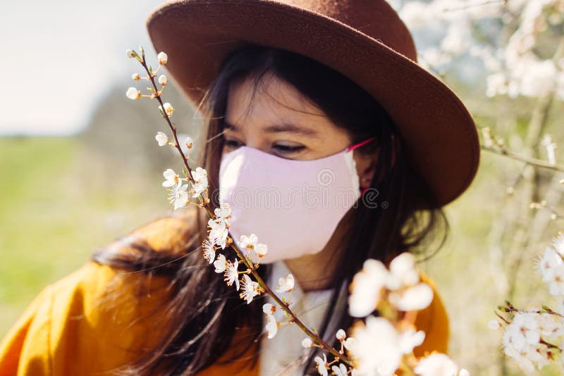 Beautiful blooming cherry tree branch  in sunny light on background of blurred stylish hipster girl wearing face mask. Tender royalty free stock image