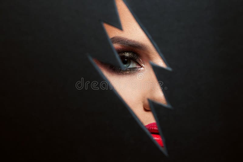Beautiful female eye with color makeup. Cutout in paper in the form of a lightning. Free space stock photography