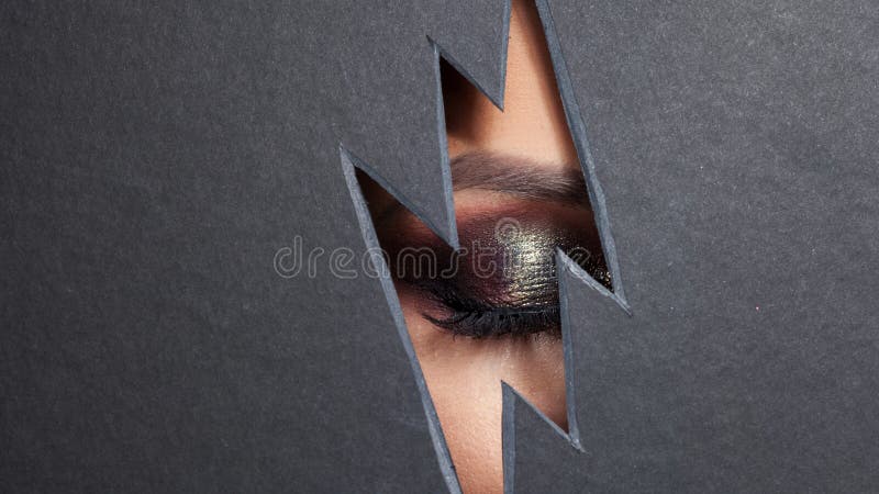 Beautiful female eye with color makeup. Cutout in paper in the form of a lightning. Free space stock photos