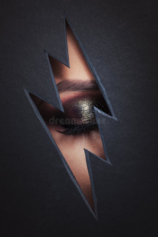 Beautiful female eye with color makeup. Cutout in paper in the form of a lightning. Free space royalty free stock image