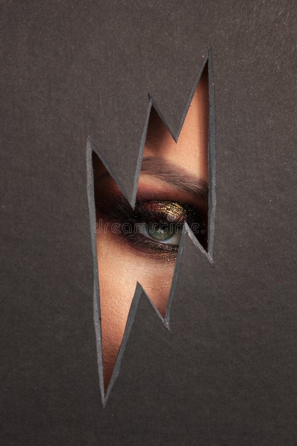 Beautiful female eye with color makeup. Cutout in paper in the form of a lightning. Free space stock images