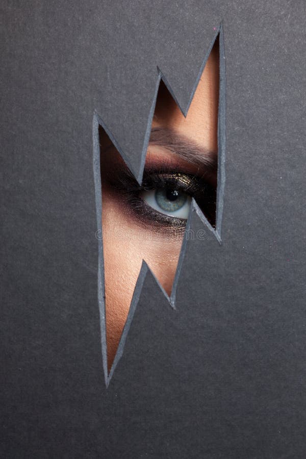Beautiful female eye with color makeup. Cutout in paper in the form of a lightning. Free space stock photography