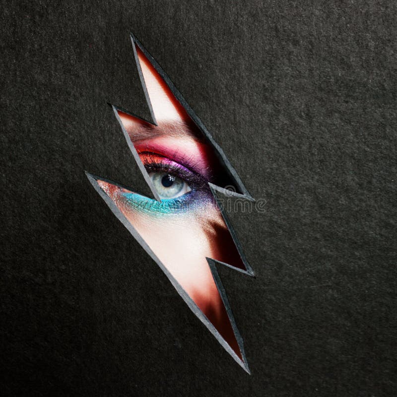 Beautiful female eye with color makeup. Cutout in paper in the form of a lightning. Free space on the right stock image