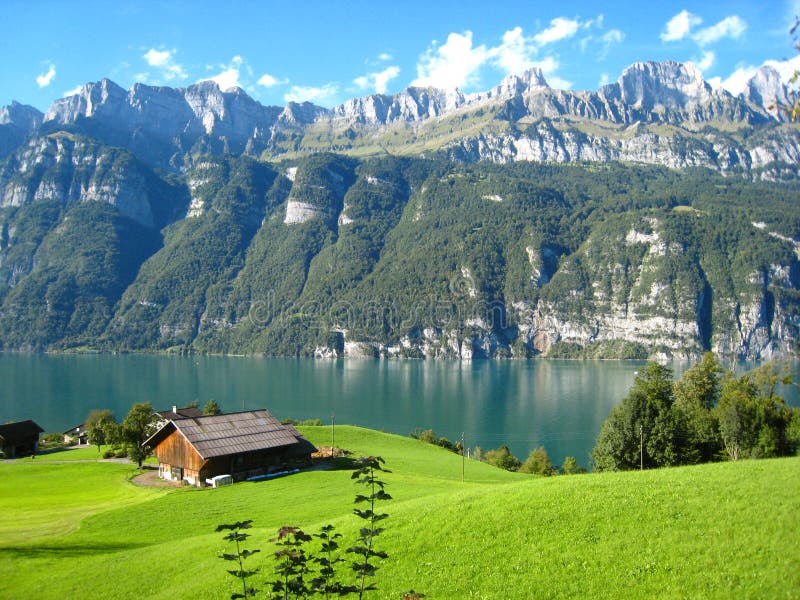 Beautifully view with a turquoise blue swiss lake with snow-covered mountains and wooden houses. Wonderfully panorama view with a turquoise blue swiss lake with stock image