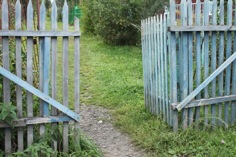 A blue old ragged gate to a dacha garden in a village with ground and grass and trees royalty free stock photo