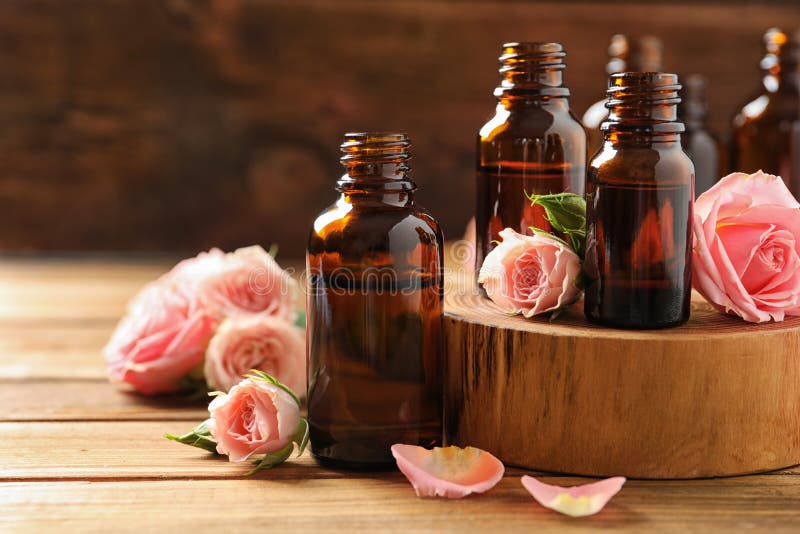 Bottles of rose essential oil and fresh flowers on wooden table stock photo