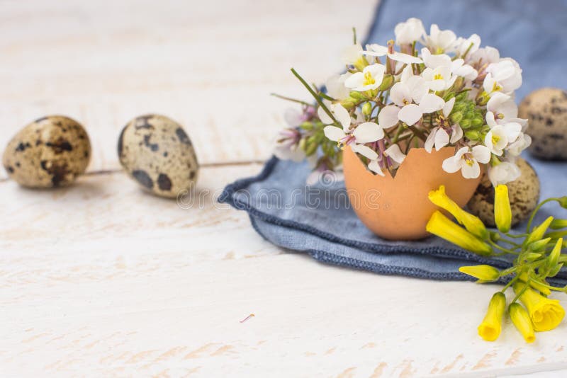 Bouquet of white yellow flowers in eggshell, quail eggs, blue napkin on wood table, Easter interior decoration stock images