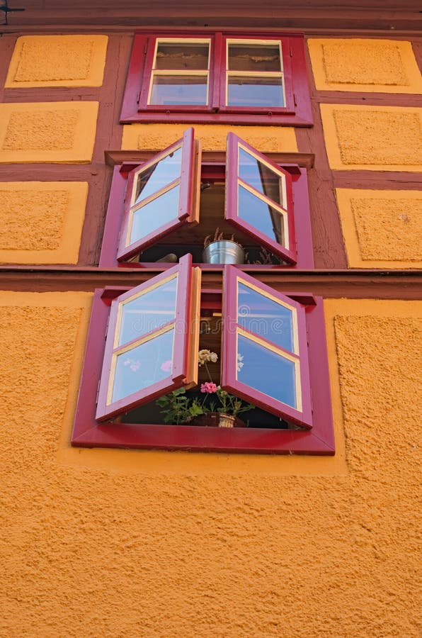 Bright yellow orange wall of rustic old house with three windows and fresh flowers. Loket, Czech Republic royalty free stock photo