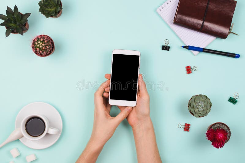 Business flatlay arrangement with woman`s hands holding smartphone with black copyspace and other stationary and office accessori. Es. Mint background. Business stock photography