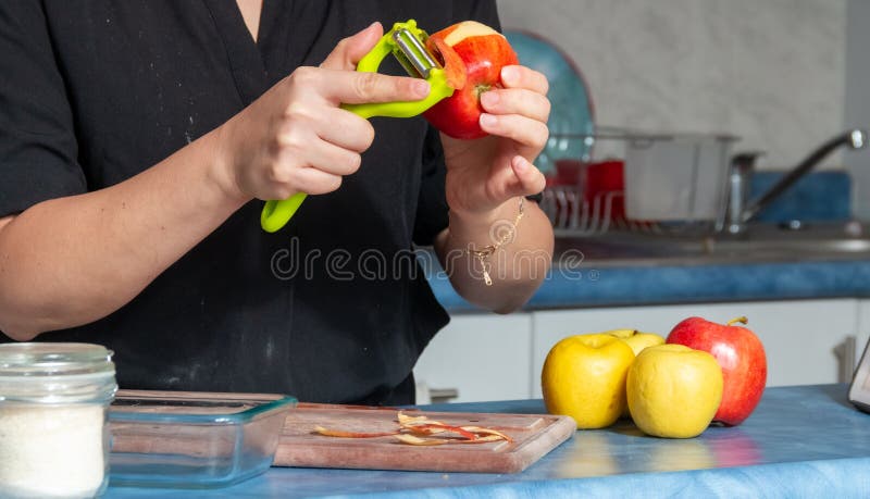 Cheerful real young woman peeling apples for a cake in the kitchen at home royalty free stock photo