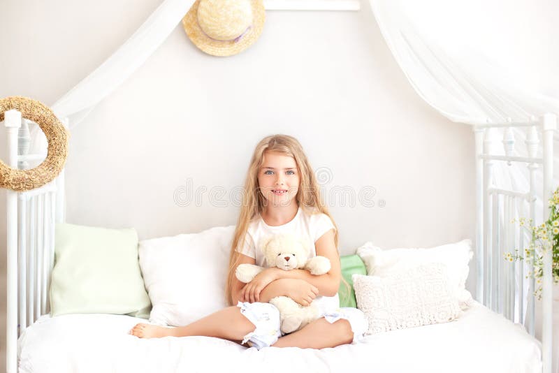 Childhood concept. Child playing in bed in a white bedroom. Children`s room and interior design. Little girl in pajamas at home. T. Oddler with a toy. sleep time royalty free stock image