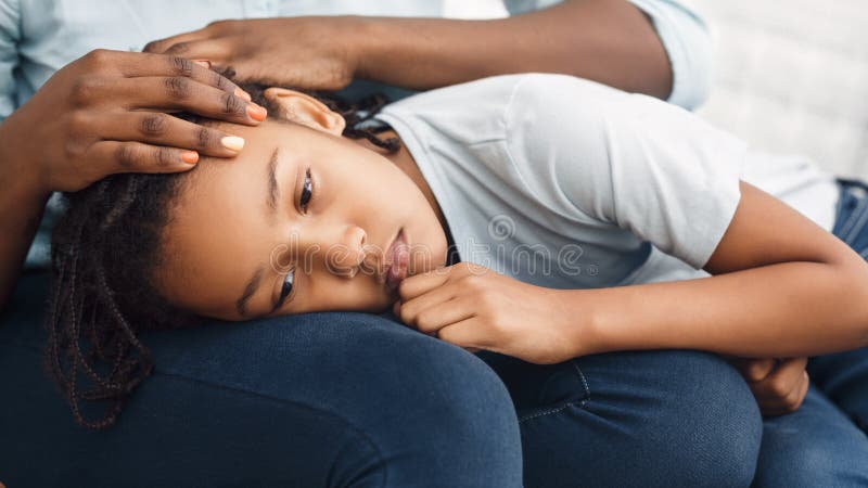 Close-up of black girl`s head laying on lap. Close-up Of Girl`s Head On Lap, African Mother Comforting Her Sad Child On Sofa At Home, Panorama stock images