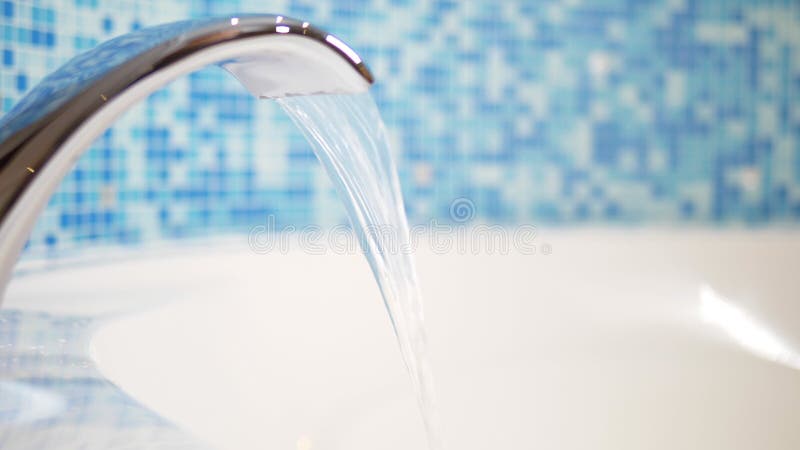 Close-up. water flows from a luxurious water tap into a large modern bathtub against a blue mosaic wall stock photos
