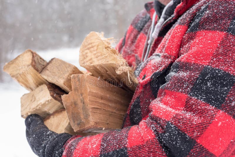 Closeup of man carrying bundle of firewood through the snow. Closeup of man in red plaid jacket carrying bundle of firewood through the snow on a cold winter day royalty free stock images