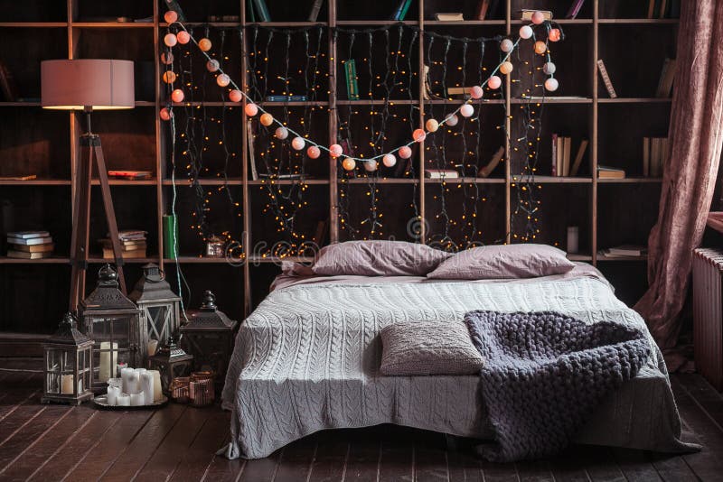 Coziness, comfort, interior and holidays concept - cozy bedroom with bed and garland lights at home. A rack with books stock photography