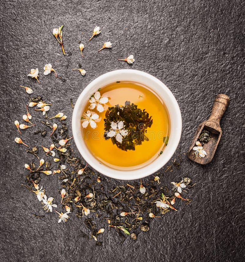 Cup of Jasmine tea, old wooden scoop and fresh flowers on dark stone background royalty free stock photography