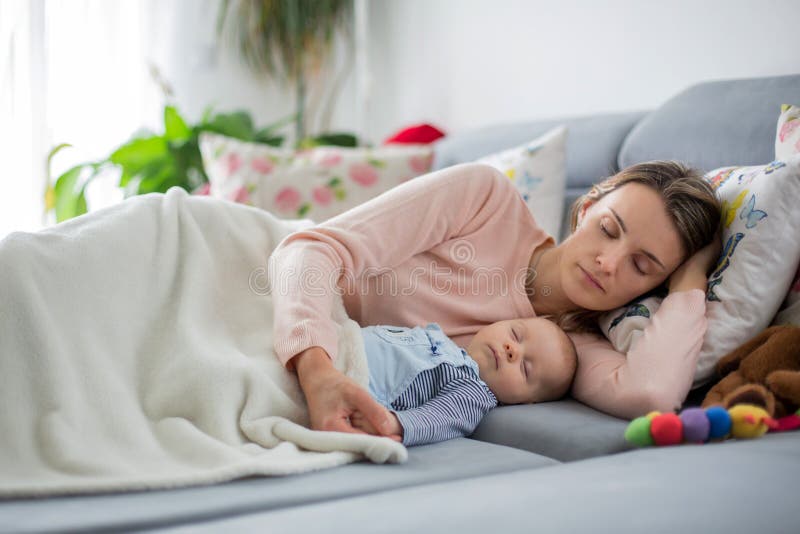 Cute baby boy and his mother, lying on the couch in living room stock photography