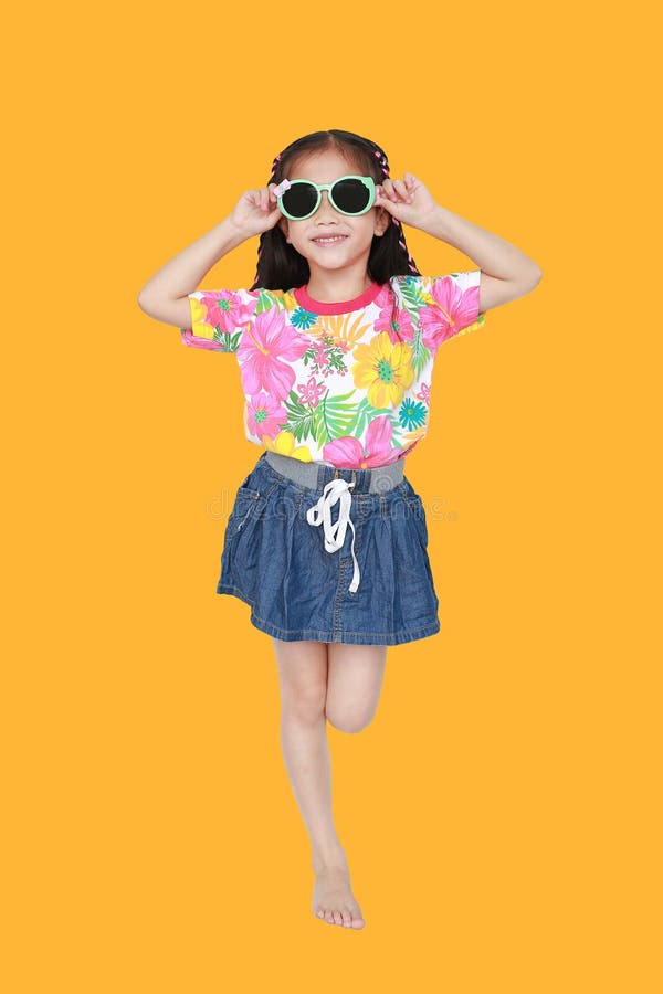 Cute little Asian kid girl wearing a flowers summer dress and sunglasses isolated on yellow background. Summer and fashion concept royalty free stock photo
