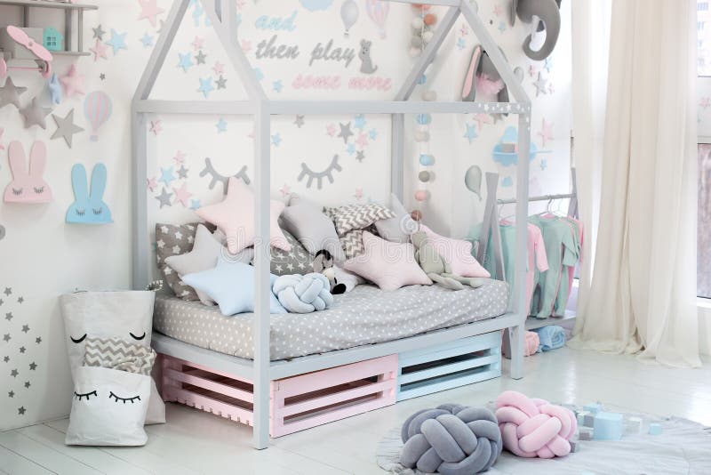 Empty cozy children`s room with a white wall with stickers, toys, a bed with pillows. Scandinavian interior of a children`s room. Wooden bed in the shape of royalty free stock photography