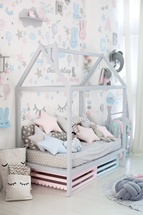 Empty cozy children`s room with a white wall with stickers, toys, a bed with pillows. Scandinavian interior of a children`s room. Wooden bed in the shape of stock photos