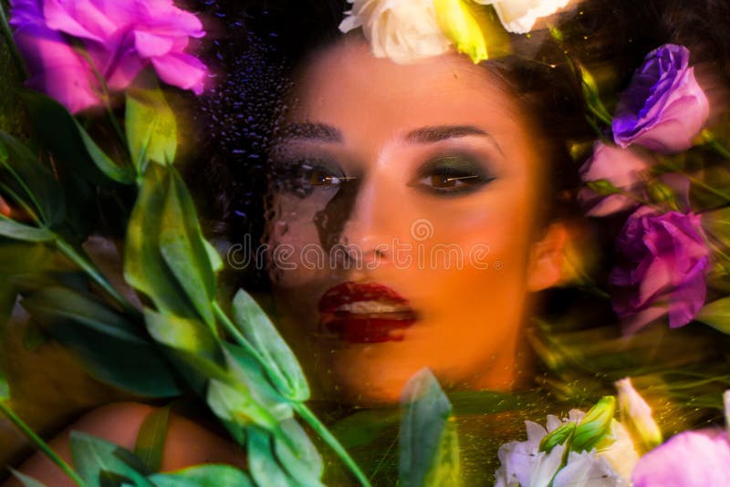 Fashion portrait of beautiful girl with bright make up among eustomas. Fashion portrait of beautiful brunette girl with bright make up looking at camera through stock image