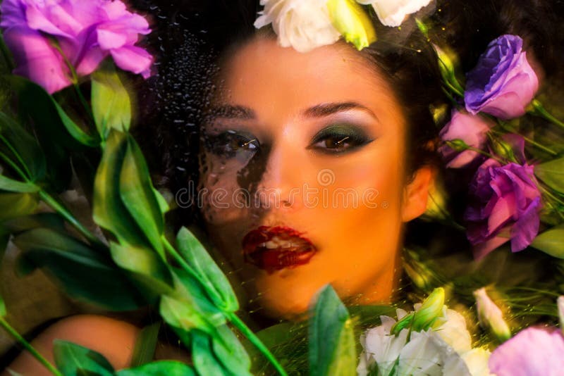 Fashion portrait of beautiful girl with bright make up among eustomas. Fashion portrait of beautiful brunette girl with bright make up looking at camera through royalty free stock photography