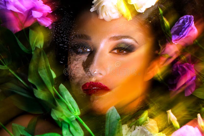 Fashion portrait of beautiful girl with bright make up among eustomas. Fashion portrait of beautiful brunette girl with bright make up looking at camera through royalty free stock images