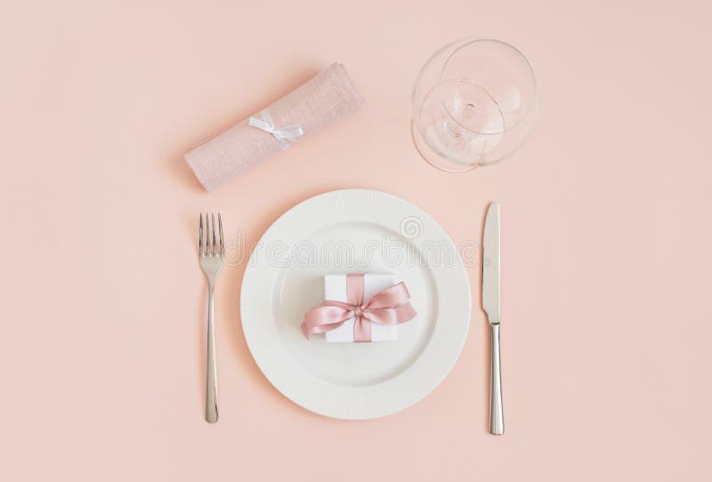 Festive table setting with a gift in a plate and cutlery on a pink background. Romantic or wedding dinner. Valentines day or royalty free stock image