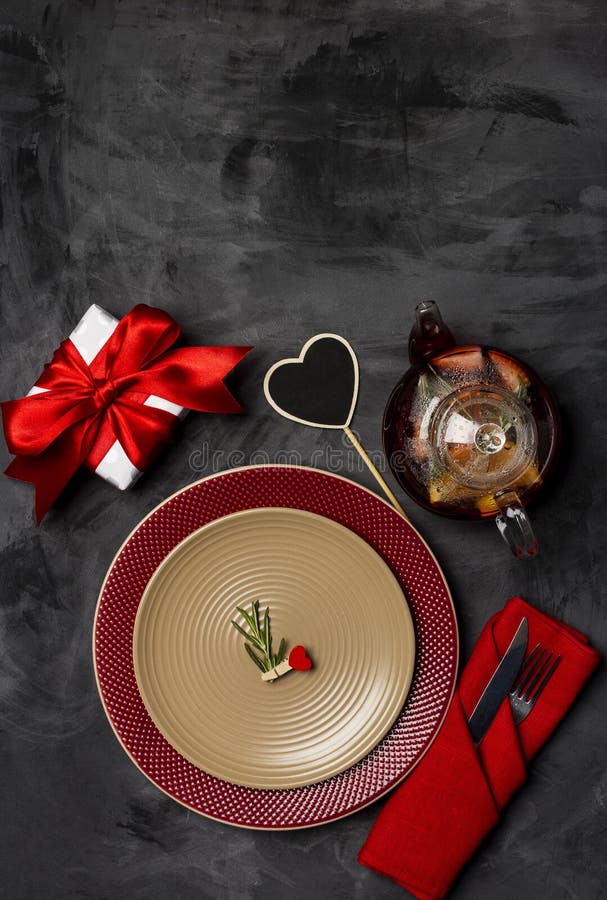 Festive table setting for Valentine`s Day with fork, knife and heart pin with rosemary at plates on a black table. Top view stock images