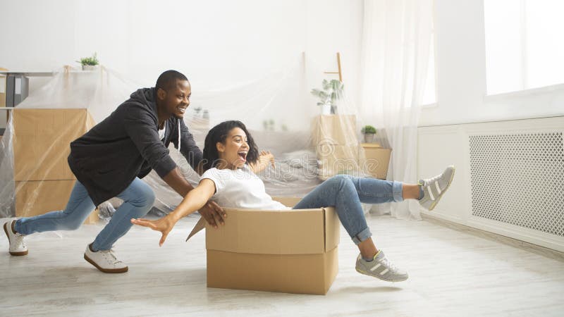 African american husband rolling his wife in cardboard box. Fun during renovations in apartment. African american husband rolling his wife in cardboard box royalty free stock photos
