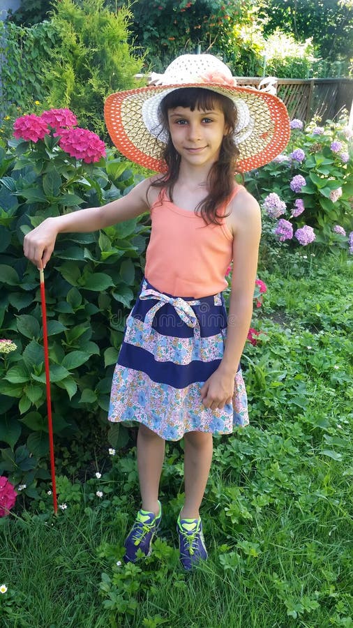 The girl in a summer hat stands near a bush of the blossoming hydrangea on the seasonal dacha.  royalty free stock photography