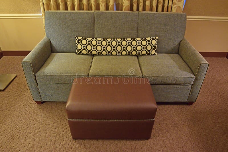 Grey Fabric Sofa with Brown Leather ottoman and long narrow pillow. Of octagon pattern. The room is furnished with curtain and carpet stock photos Grey Fabric Sofa with Brown Leather ottoman and long narrow pillow. Of octagon pattern. The room is furnished with curtain and carpet stock photos