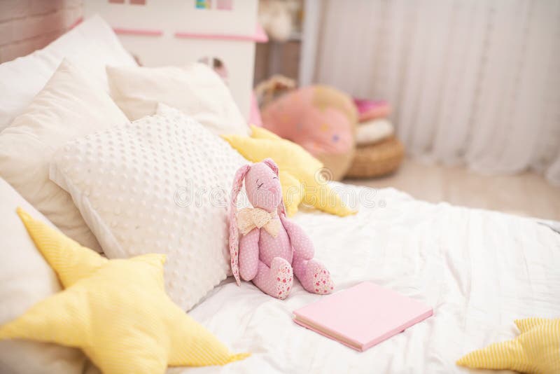 Handmade plush rabbit made of fabric sits on a cozy bed in the children `s room. Nursery there is a Dollhouse and a lot of toys. On the bed there are a lot of royalty free stock photo