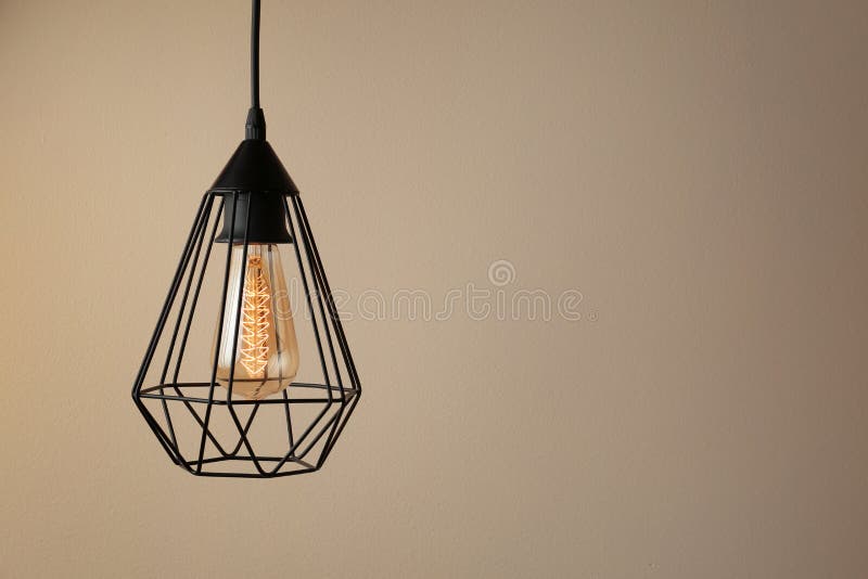 Hanging lamp bulb in chandelier against beige background. Space for text stock images