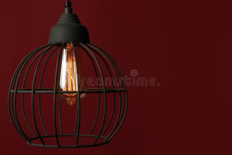 Hanging lamp bulb in chandelier against dark red background. Space for text stock photography