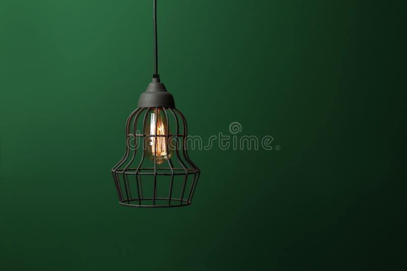 Hanging lamp bulb in chandelier against green background. Space for text royalty free stock image