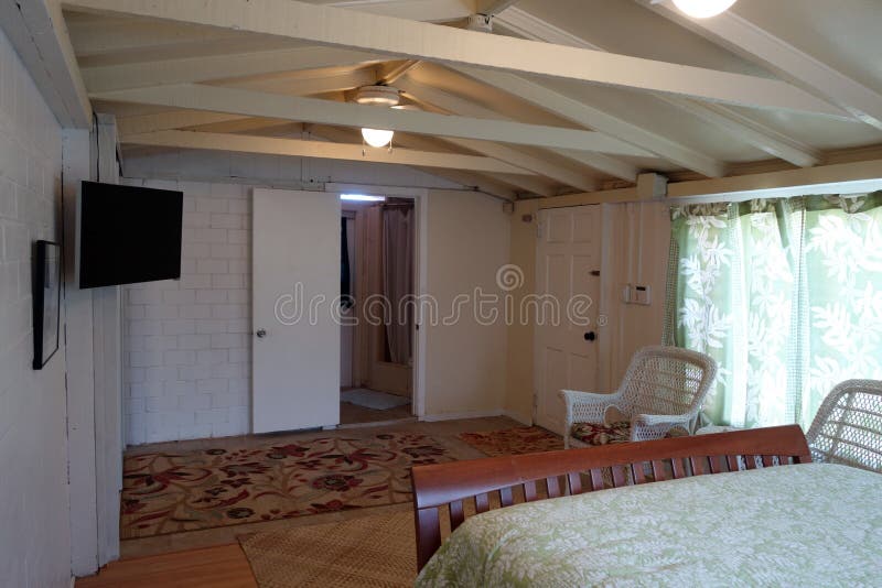 Inside Cottage Bedroom. With Queen bed, Mounted HDTV, White Wicker chairs and bathroom royalty free stock photo