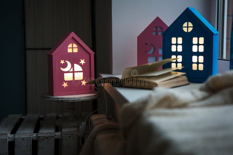 The interior of the children`s room, cozy night lights in the form of houses on the window glow yellow. A cozy windowsill of a children`s room with a night royalty free stock photo