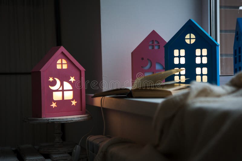 The interior of the children`s room, cozy night lights in the form of houses on the window glow yellow. A cozy windowsill of a children`s room with a night stock photography