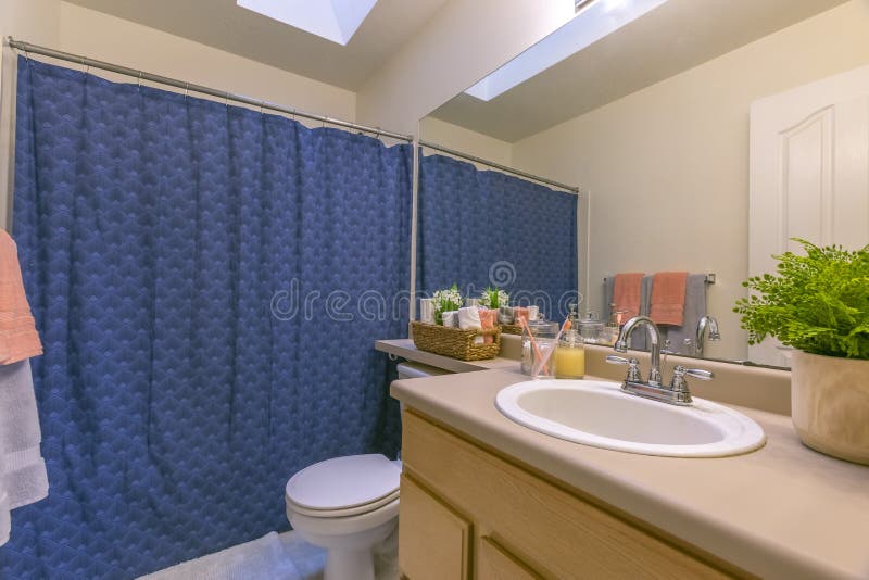 Interior of a small and cozy bathroom with a single vanity unit and toilet. The blue shower curtain conceals the shower and bathtub stock images
