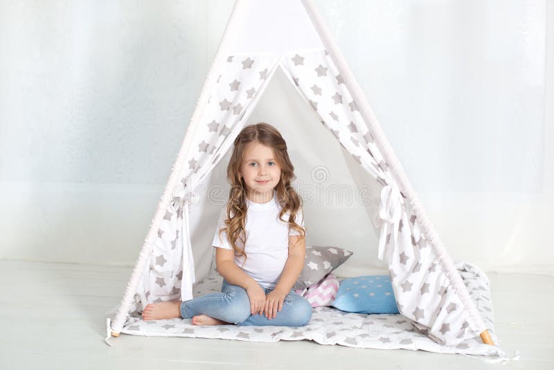 Kid prepare to go to bed. Pleasant time in cozy bedroom. A little girl sits in a tepee with colorful pillows in her room. Decorati. Ng a children`s room with a royalty free stock photography